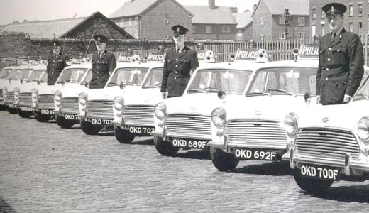 A long line of Liverpool police Minis on a cobbled street